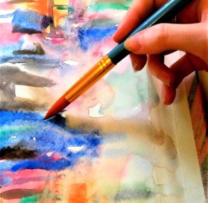 hand holding paint brush touching watercolour painting